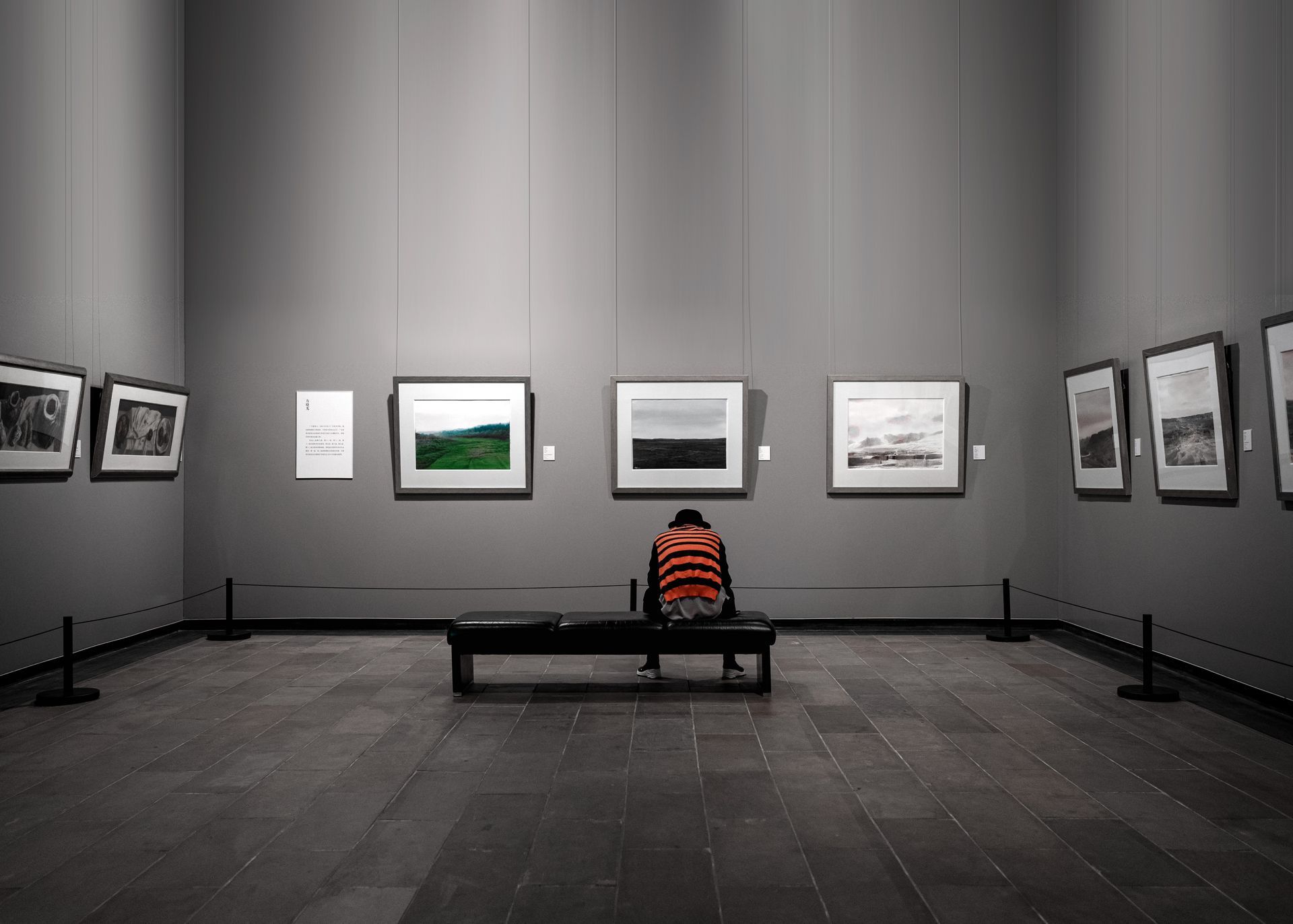 A person is sitting on a bench in a museum looking at paintings.