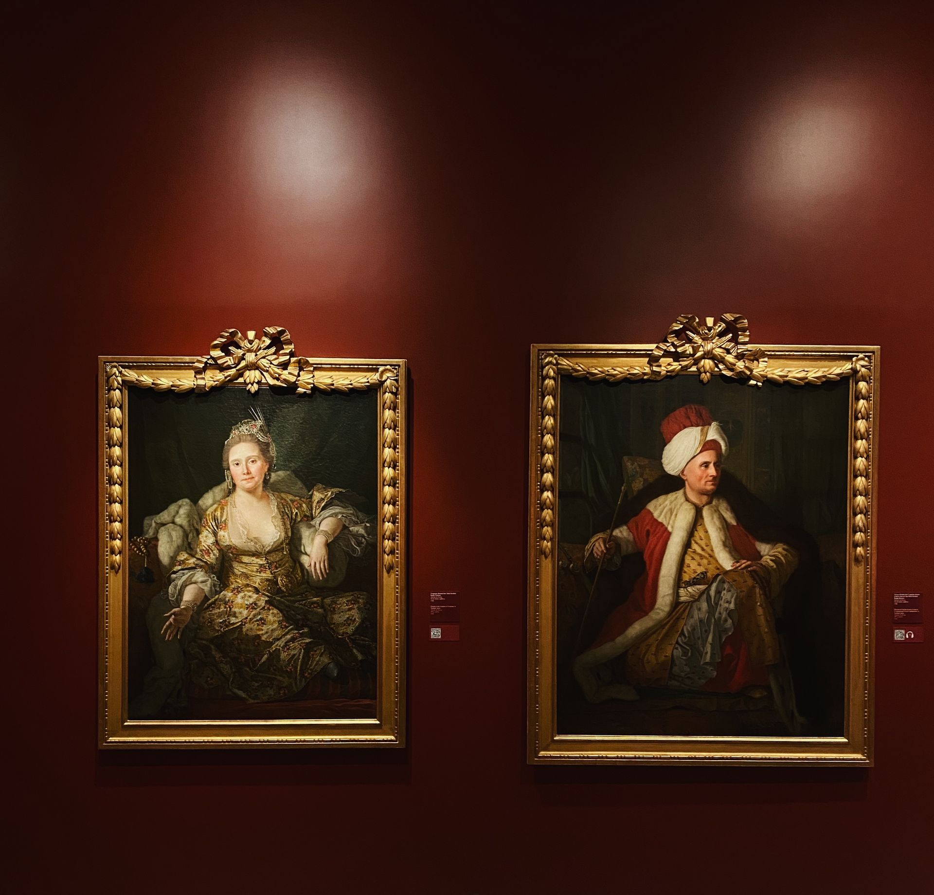 Two paintings of a woman and a man are hanging on a red wall
