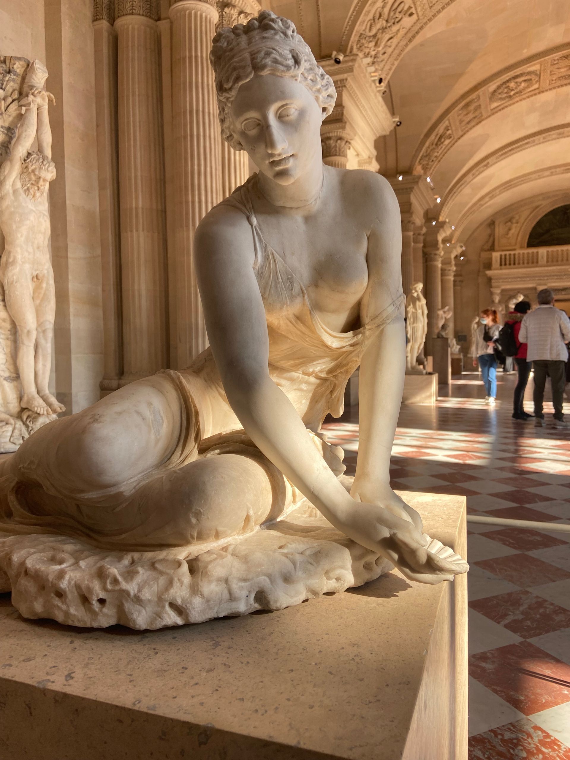 A statue of a woman is sitting on a pedestal in a museum.