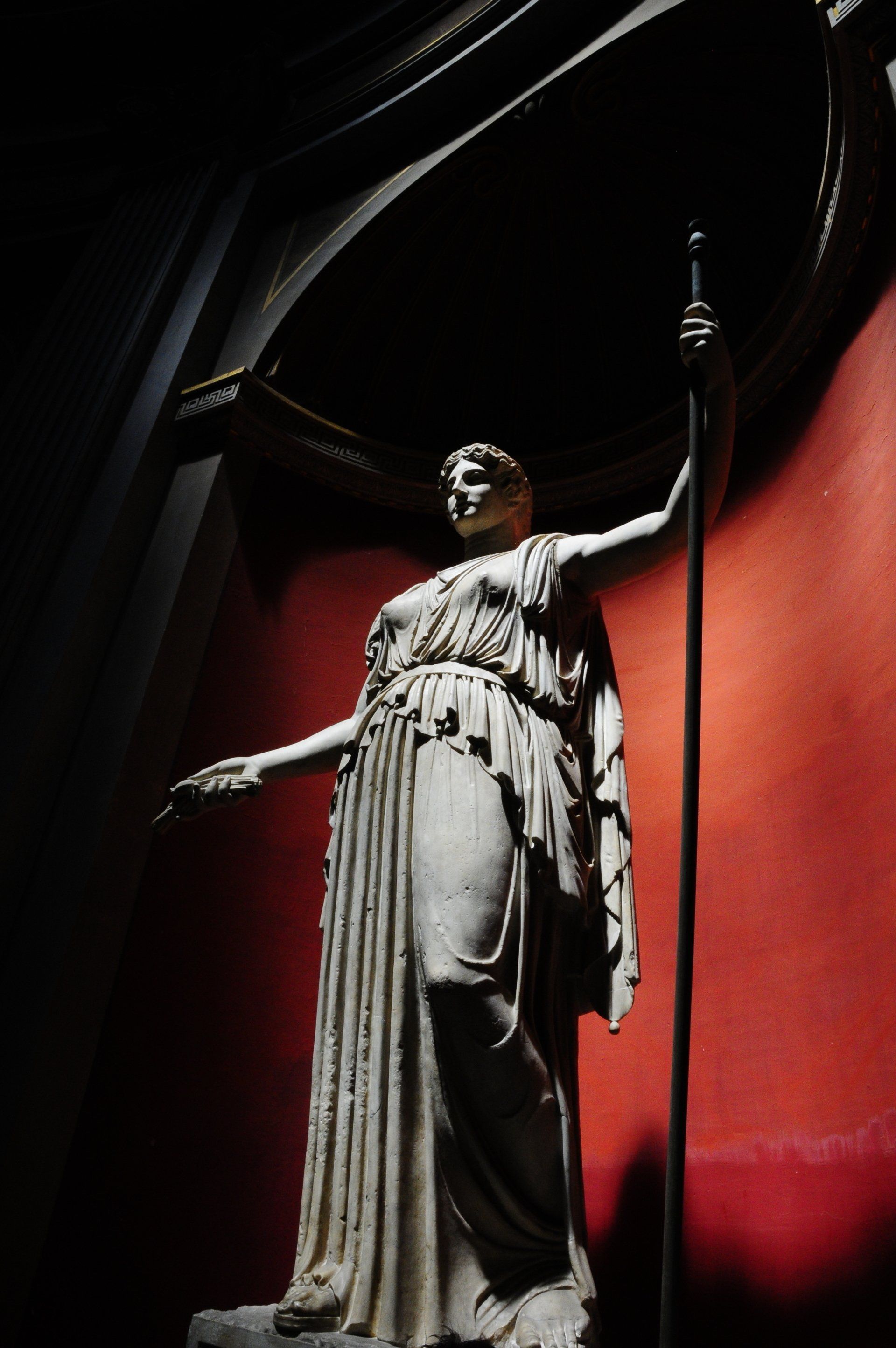 A statue of a woman holding a pole in front of a red wall