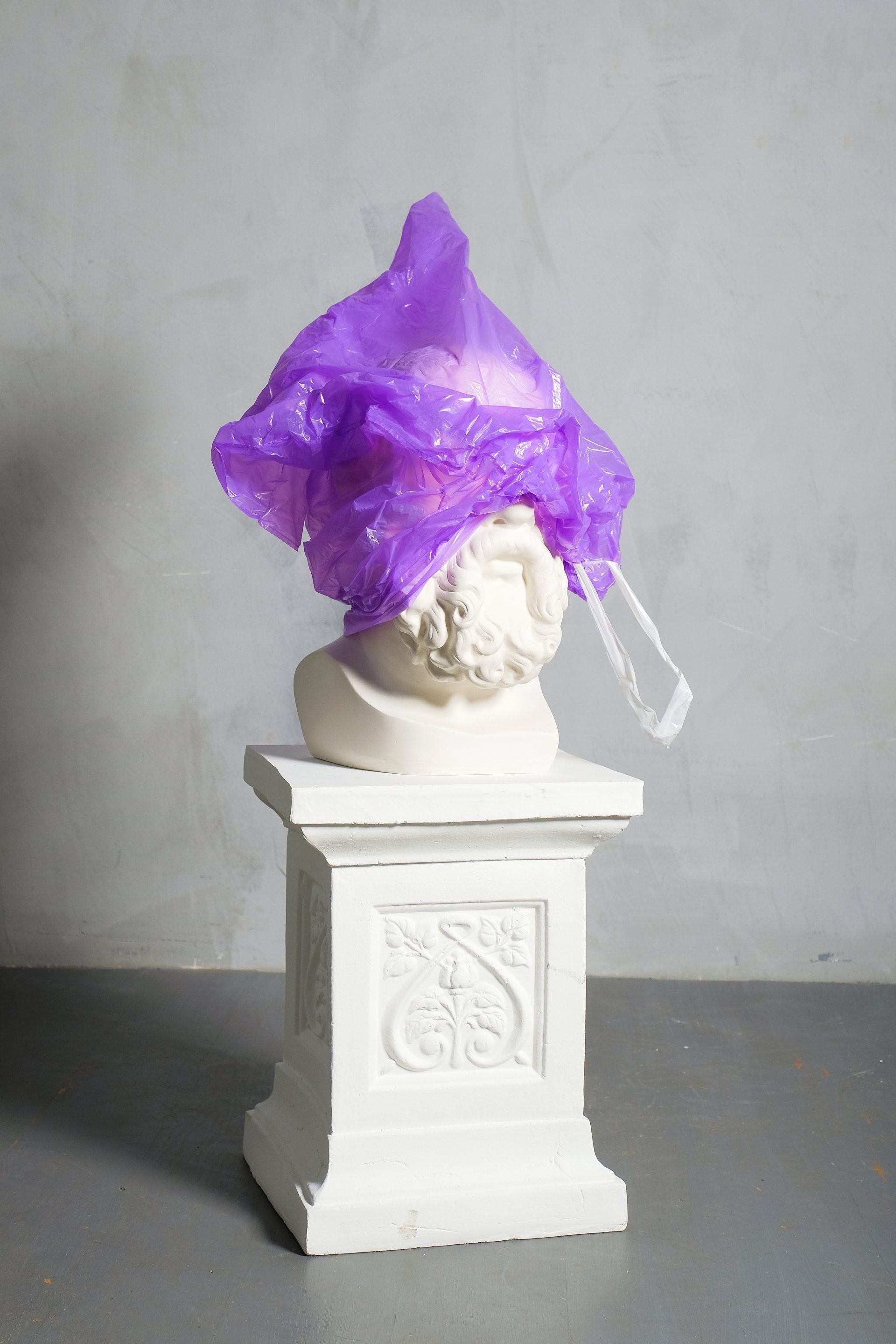 A statue of a man with a purple plastic bag on top of it.