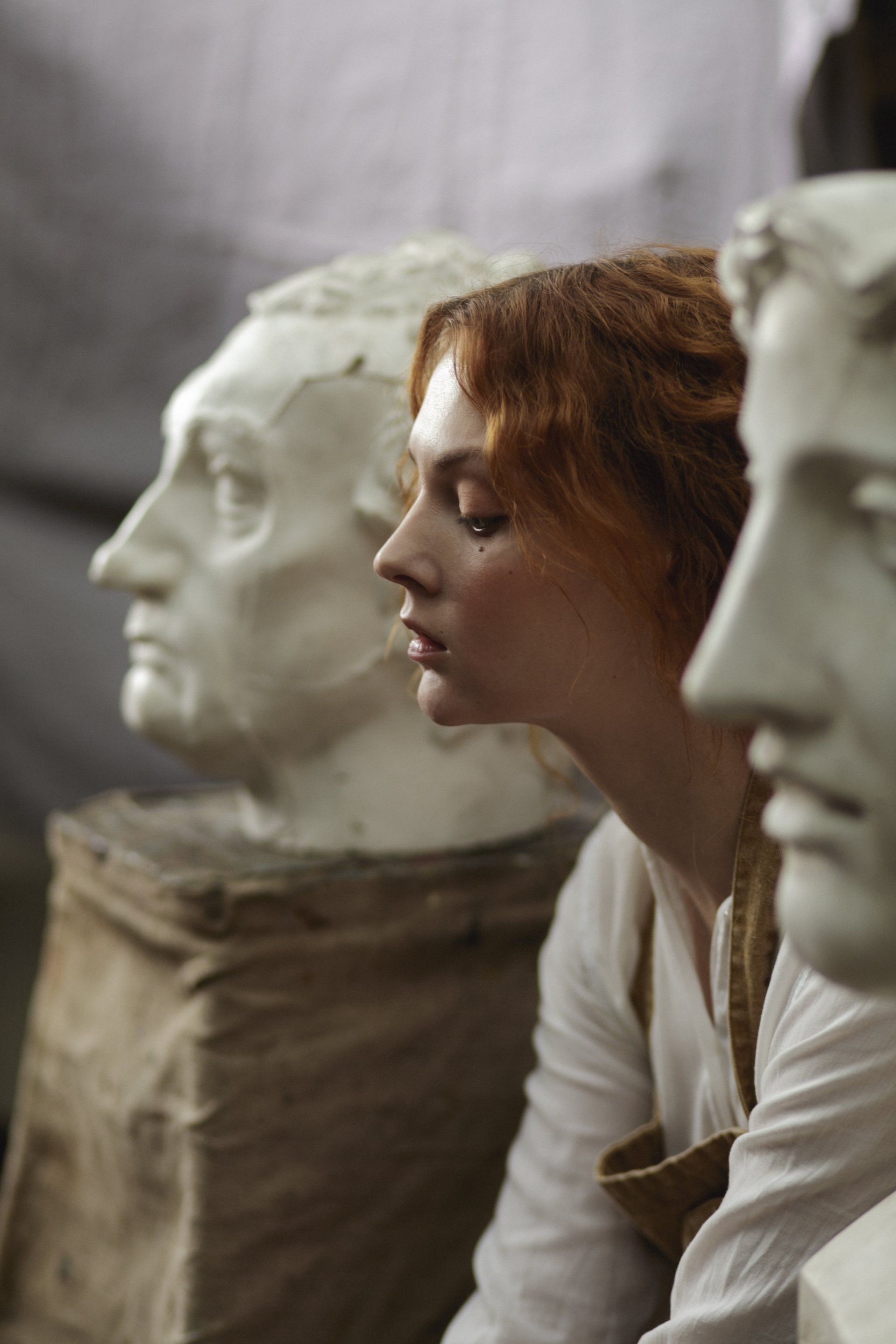 A woman is sitting next to a statue of a man 's head.