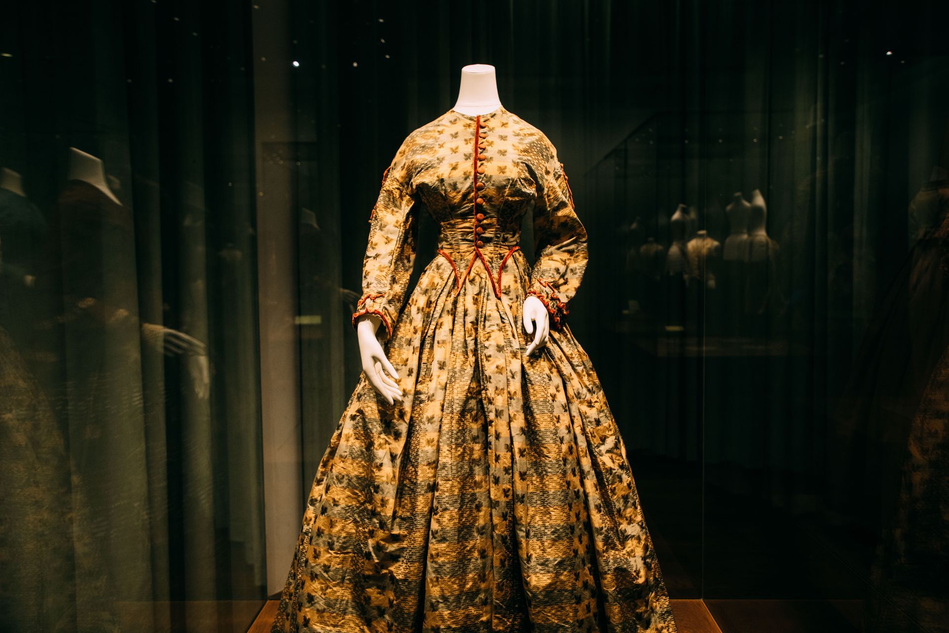 A mannequin is wearing a gold dress in a museum.