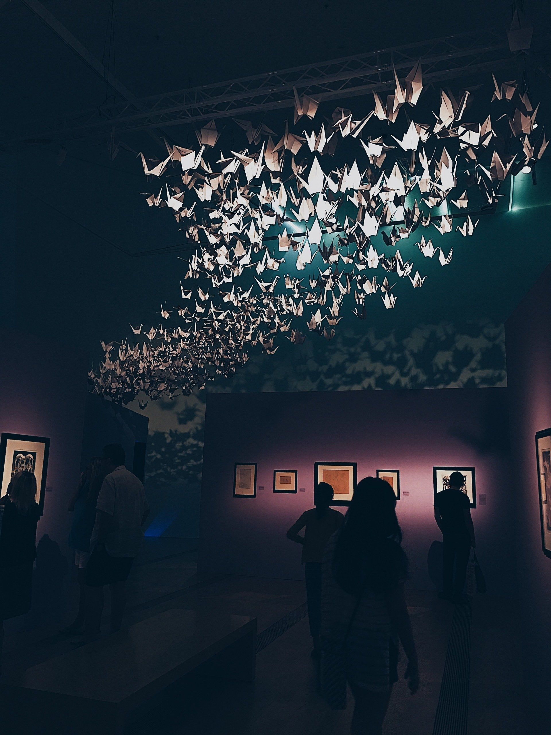 A group of people are standing in a dark room looking at paintings on the wall.
