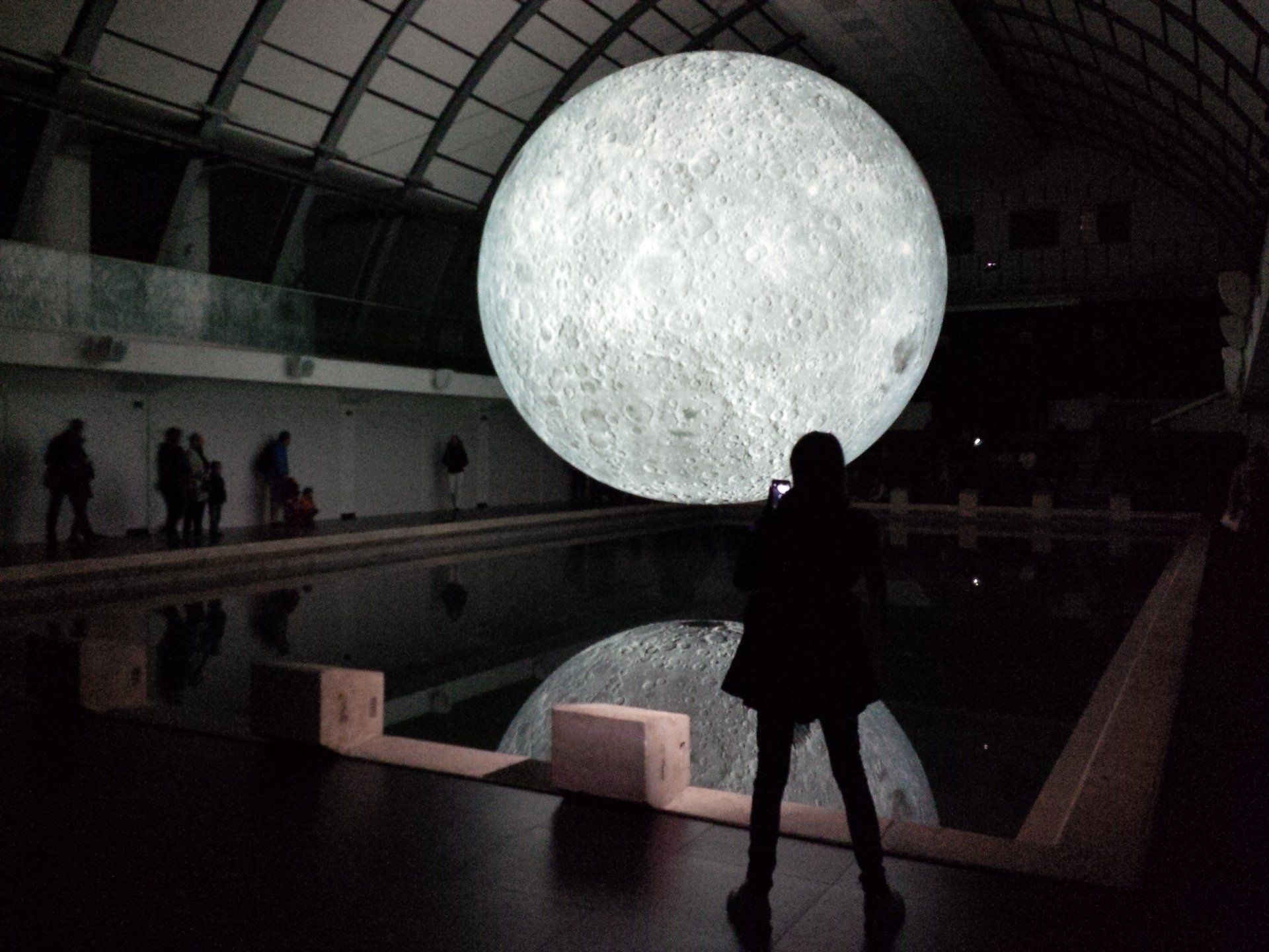 A woman stands in front of a giant moon in a dark room